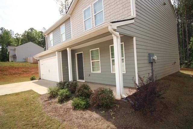 view of side of home featuring covered porch, an attached garage, and concrete driveway