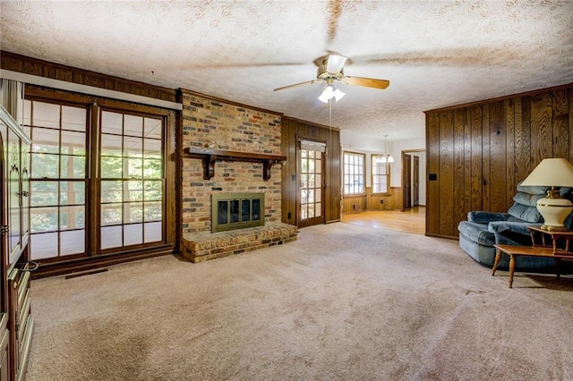 carpeted living room featuring a fireplace, wood walls, a textured ceiling, and ceiling fan