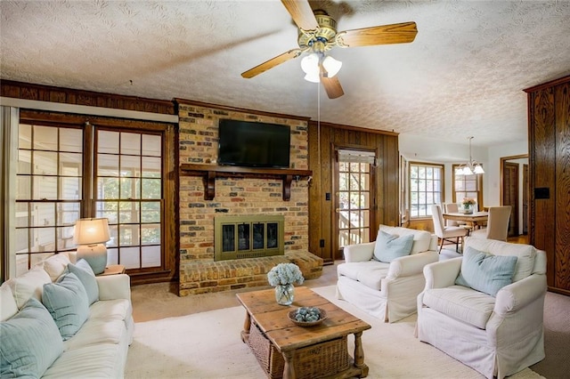 carpeted living room with wood walls, a textured ceiling, a brick fireplace, and ceiling fan with notable chandelier