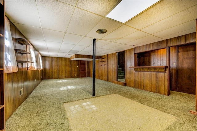 basement with wooden walls, a drop ceiling, and carpet