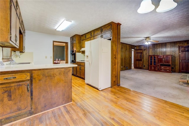 kitchen featuring white refrigerator with ice dispenser, a textured ceiling, wood walls, oven, and light hardwood / wood-style flooring