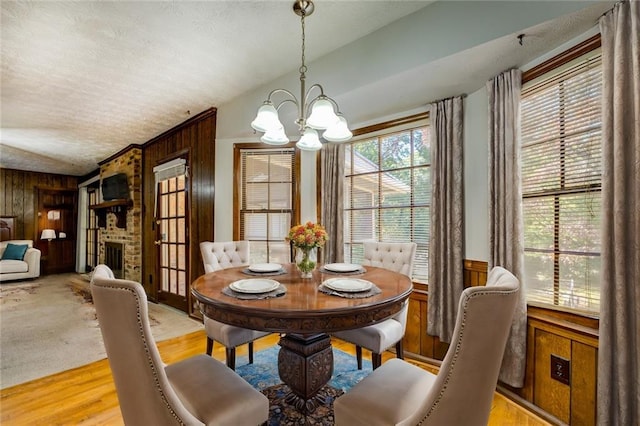 dining space with a fireplace, wood walls, lofted ceiling, and light hardwood / wood-style flooring