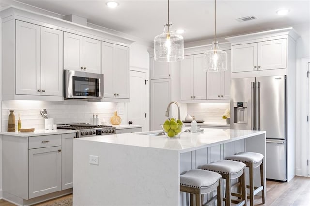 kitchen with stainless steel appliances, tasteful backsplash, light hardwood / wood-style flooring, an island with sink, and hanging light fixtures