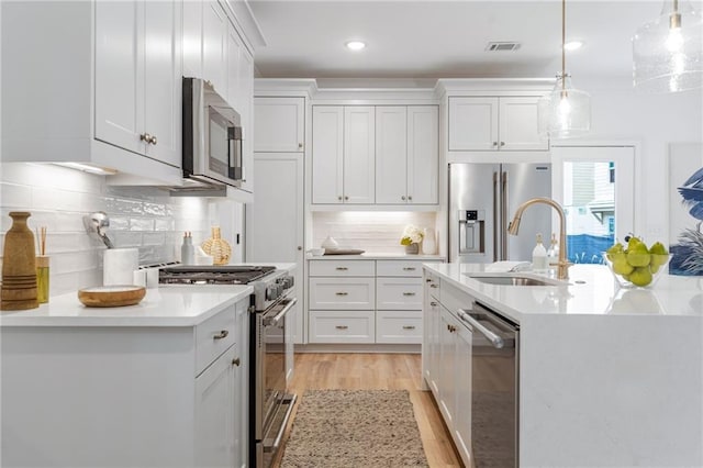 kitchen featuring a kitchen island with sink, stainless steel appliances, hanging light fixtures, white cabinetry, and backsplash