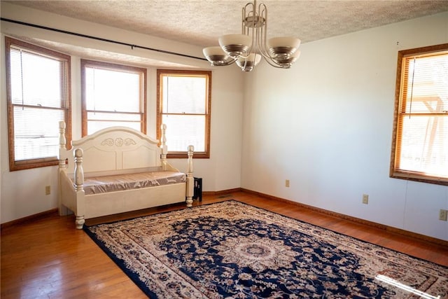 bedroom with hardwood / wood-style floors, a textured ceiling, and a notable chandelier