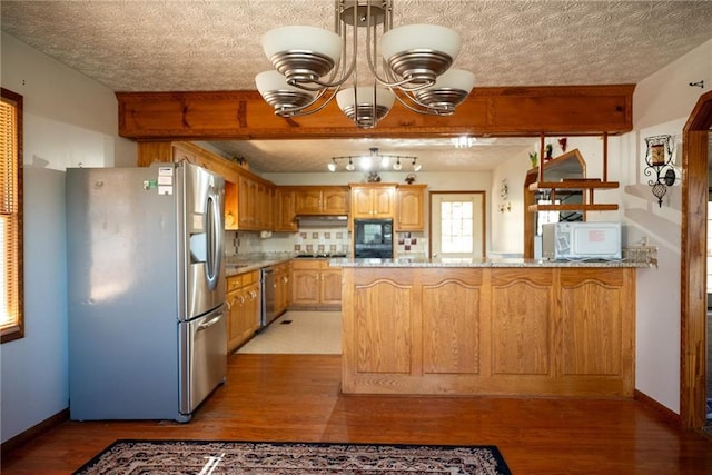 kitchen with light stone countertops, light wood-type flooring, appliances with stainless steel finishes, tasteful backsplash, and kitchen peninsula