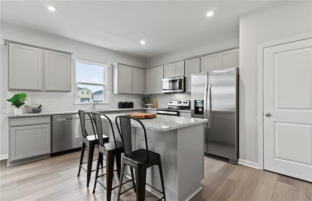 kitchen with a kitchen breakfast bar, a center island, light stone counters, stainless steel appliances, and light hardwood / wood-style flooring