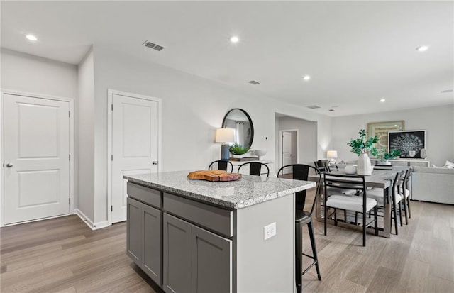 kitchen with light hardwood / wood-style flooring, light stone counters, gray cabinets, and a kitchen island