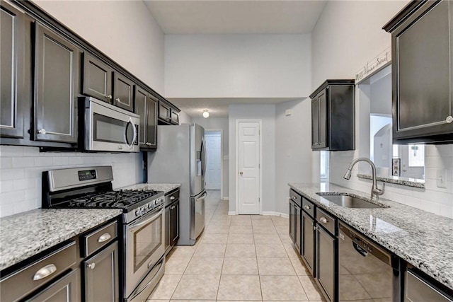 kitchen with sink, light stone countertops, light tile patterned floors, appliances with stainless steel finishes, and tasteful backsplash