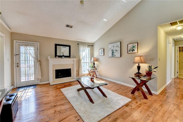 living area featuring light wood-style flooring, visible vents, a fireplace with raised hearth, and baseboards