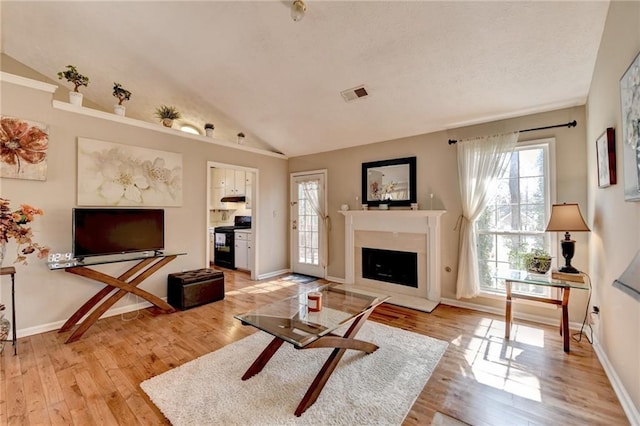 living area with lofted ceiling, light wood-type flooring, visible vents, and a fireplace with raised hearth