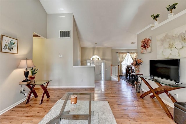 living area with a towering ceiling, wood finished floors, visible vents, and baseboards