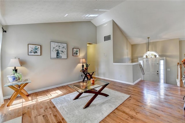 interior space with high vaulted ceiling, wood finished floors, visible vents, and baseboards