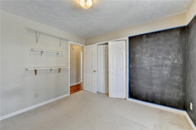 unfurnished bedroom with a textured ceiling, carpet floors, a closet, and baseboards