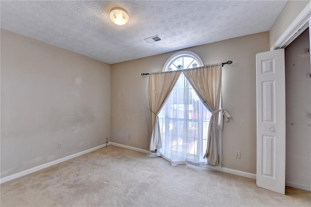 carpeted spare room with a textured ceiling, visible vents, and baseboards