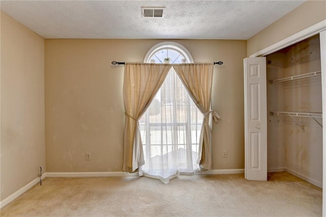 unfurnished bedroom with a textured ceiling, carpet floors, visible vents, baseboards, and a closet