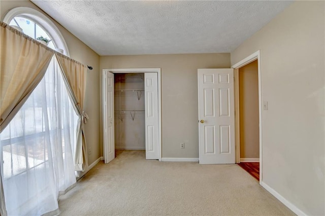 unfurnished bedroom featuring a textured ceiling, a closet, baseboards, and light colored carpet