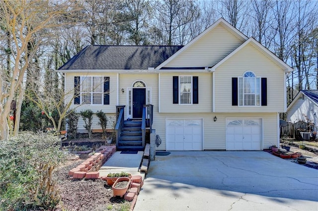 raised ranch featuring concrete driveway, a shingled roof, an attached garage, and cooling unit