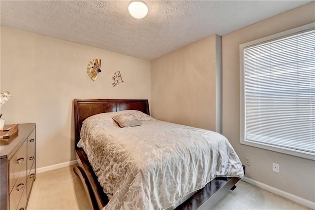 bedroom with light carpet, a textured ceiling, and baseboards