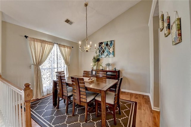 dining space featuring a notable chandelier, visible vents, vaulted ceiling, wood finished floors, and baseboards