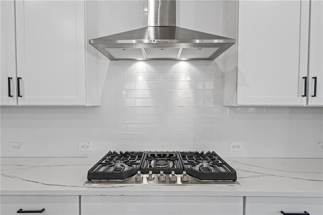 details with wall chimney range hood, white cabinetry, stainless steel gas stovetop, and tasteful backsplash