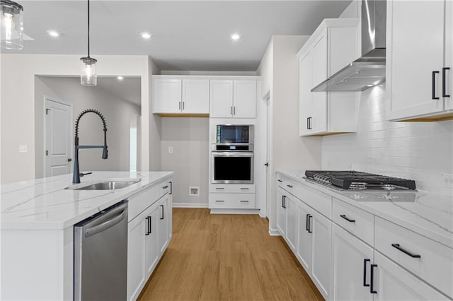 kitchen with light wood-style flooring, a sink, wall chimney exhaust hood, stainless steel appliances, and white cabinets