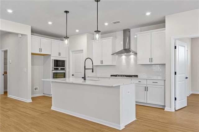 kitchen with oven, wall chimney range hood, light wood-type flooring, visible vents, and gas cooktop