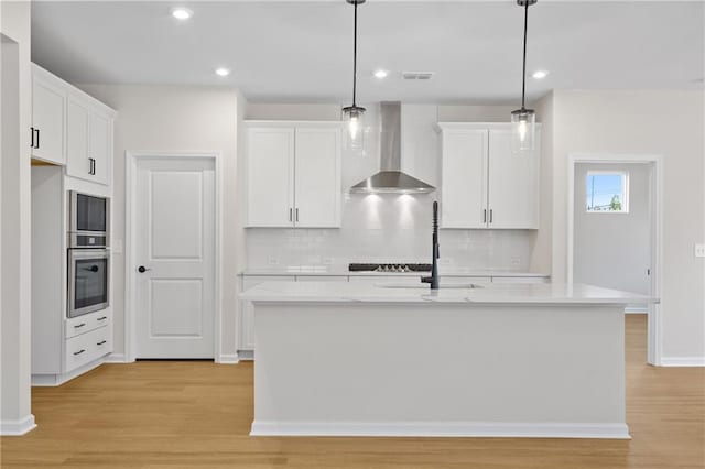 kitchen with white cabinetry, decorative backsplash, wall chimney range hood, light wood-style floors, and oven