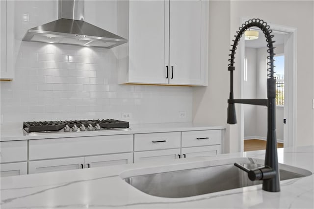 kitchen featuring wall chimney range hood, decorative backsplash, stainless steel gas cooktop, and white cabinets