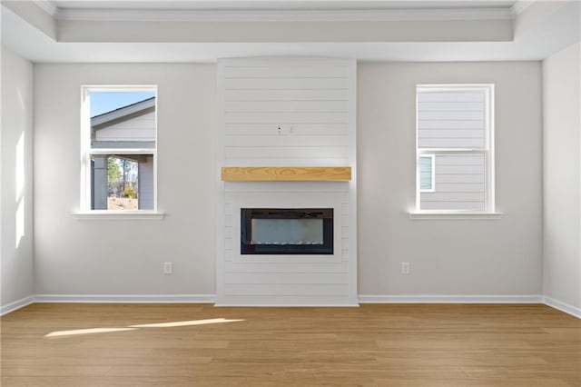 unfurnished living room with a tray ceiling, ornamental molding, and light wood-style flooring