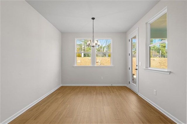 unfurnished dining area with baseboards, a notable chandelier, plenty of natural light, and wood finished floors