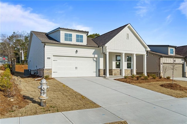 view of front facade featuring a porch, concrete driveway, stone siding, and central AC