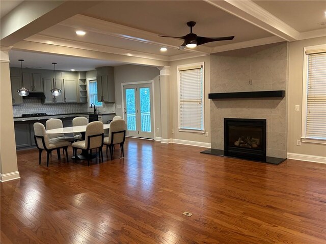 living room featuring ceiling fan, beamed ceiling, sink, a tiled fireplace, and dark hardwood / wood-style floors