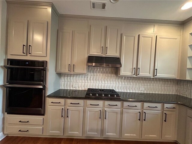 kitchen with dark wood-type flooring, backsplash, stainless steel gas cooktop, black double oven, and dark stone counters