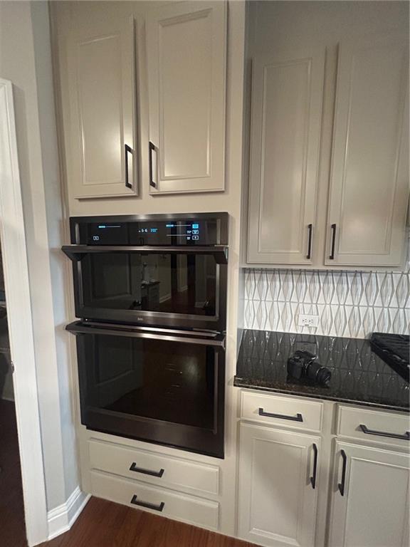 kitchen with dark stone countertops, white cabinets, black double oven, and tasteful backsplash