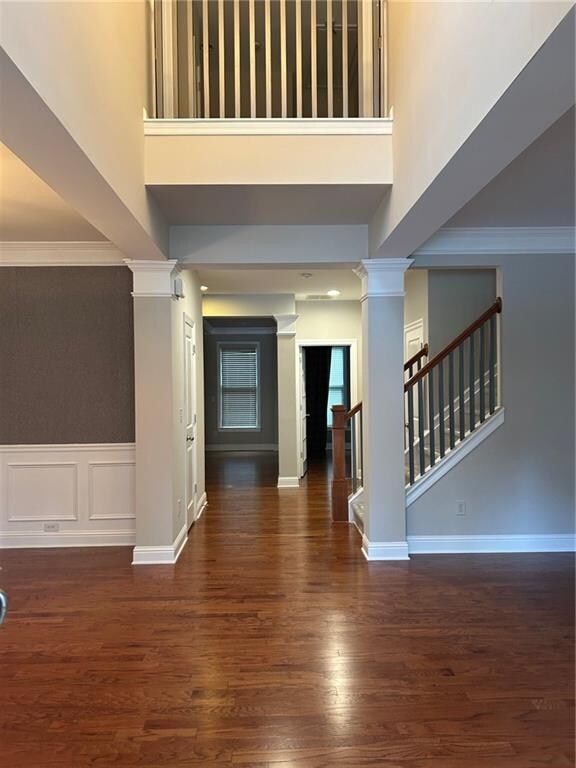 entrance foyer with ornamental molding, a towering ceiling, ornate columns, and dark hardwood / wood-style flooring