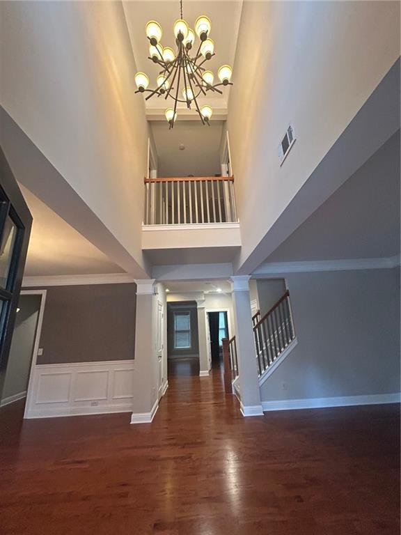 foyer with a chandelier, dark wood-type flooring, decorative columns, crown molding, and a high ceiling