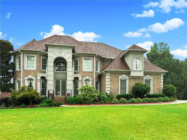 view of front of property with a front lawn, french doors, brick siding, and a shingled roof