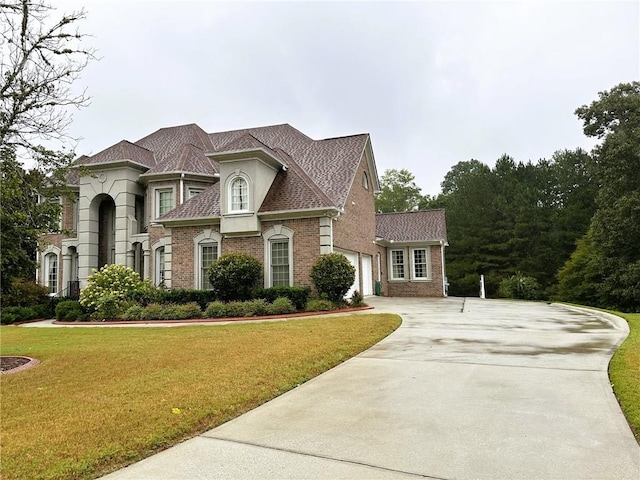 view of front of home featuring driveway, brick siding, an attached garage, and a front yard