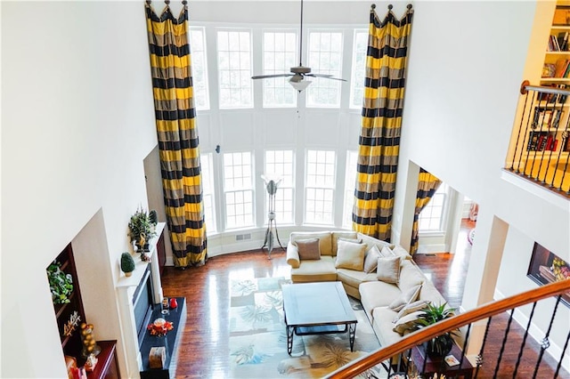 living area featuring a ceiling fan, plenty of natural light, wood finished floors, and a towering ceiling