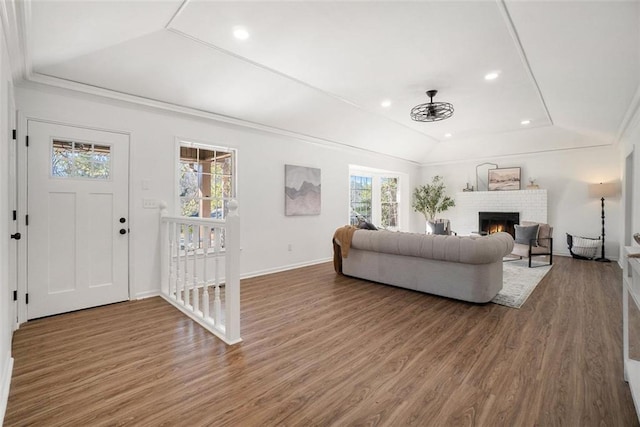 living room with wood-type flooring, ornamental molding, lofted ceiling, and a fireplace