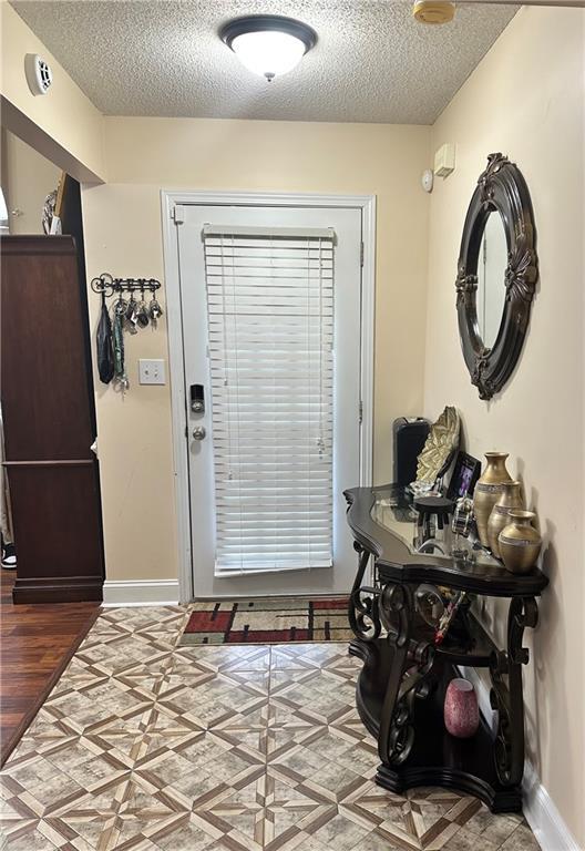 doorway featuring baseboards, a textured ceiling, and light wood-type flooring