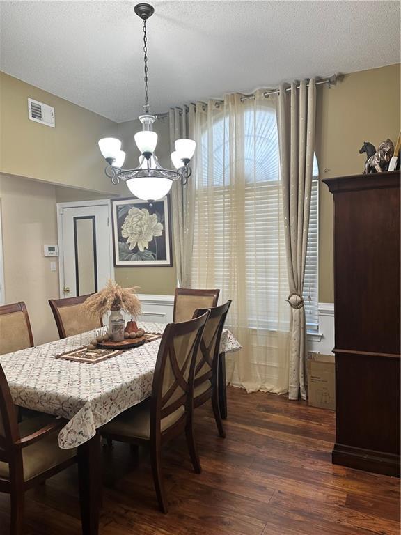 dining area featuring an inviting chandelier, a textured ceiling, dark wood-style flooring, and visible vents