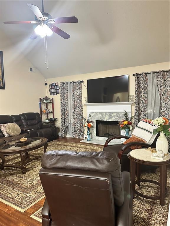 living room with a ceiling fan, wood finished floors, lofted ceiling, a high end fireplace, and visible vents