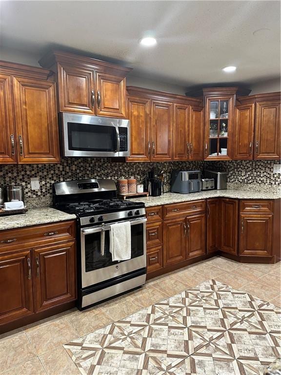 kitchen featuring light stone countertops, glass insert cabinets, recessed lighting, tasteful backsplash, and appliances with stainless steel finishes