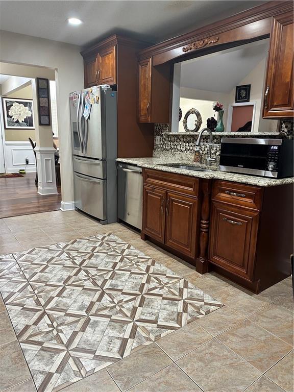 kitchen with stainless steel appliances, light stone countertops, light tile patterned floors, and a sink