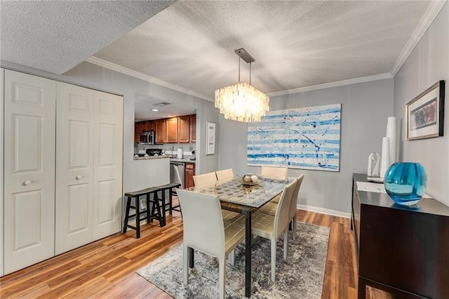 dining room with wood-type flooring, ornamental molding, a textured ceiling, and a notable chandelier