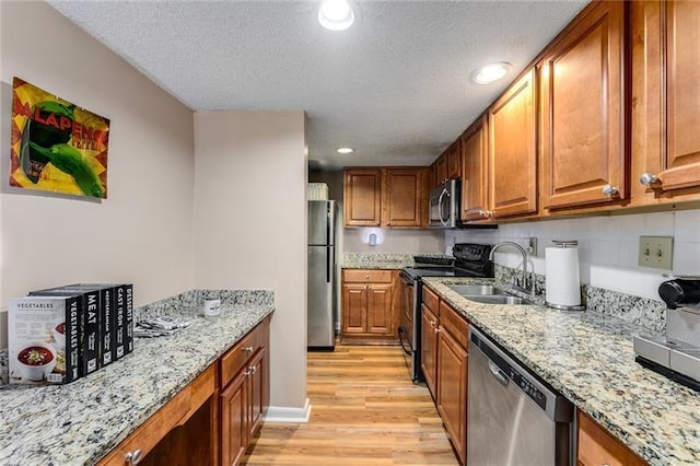 kitchen featuring light hardwood / wood-style floors, light stone countertops, sink, and appliances with stainless steel finishes