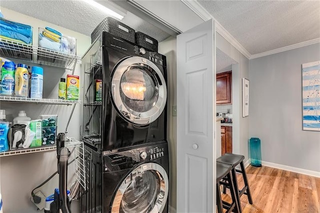 laundry room featuring light wood-type flooring, a textured ceiling, stacked washing maching and dryer, and crown molding