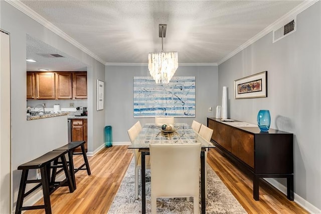 dining area with a textured ceiling, a notable chandelier, light wood-type flooring, and crown molding